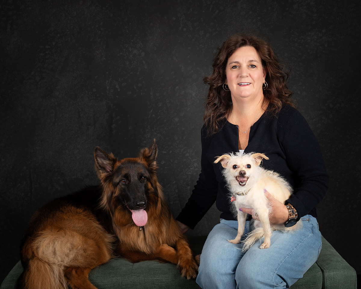 Woman sitting with two dogs, a German Shepherd and a small white dog, smiling at the camera